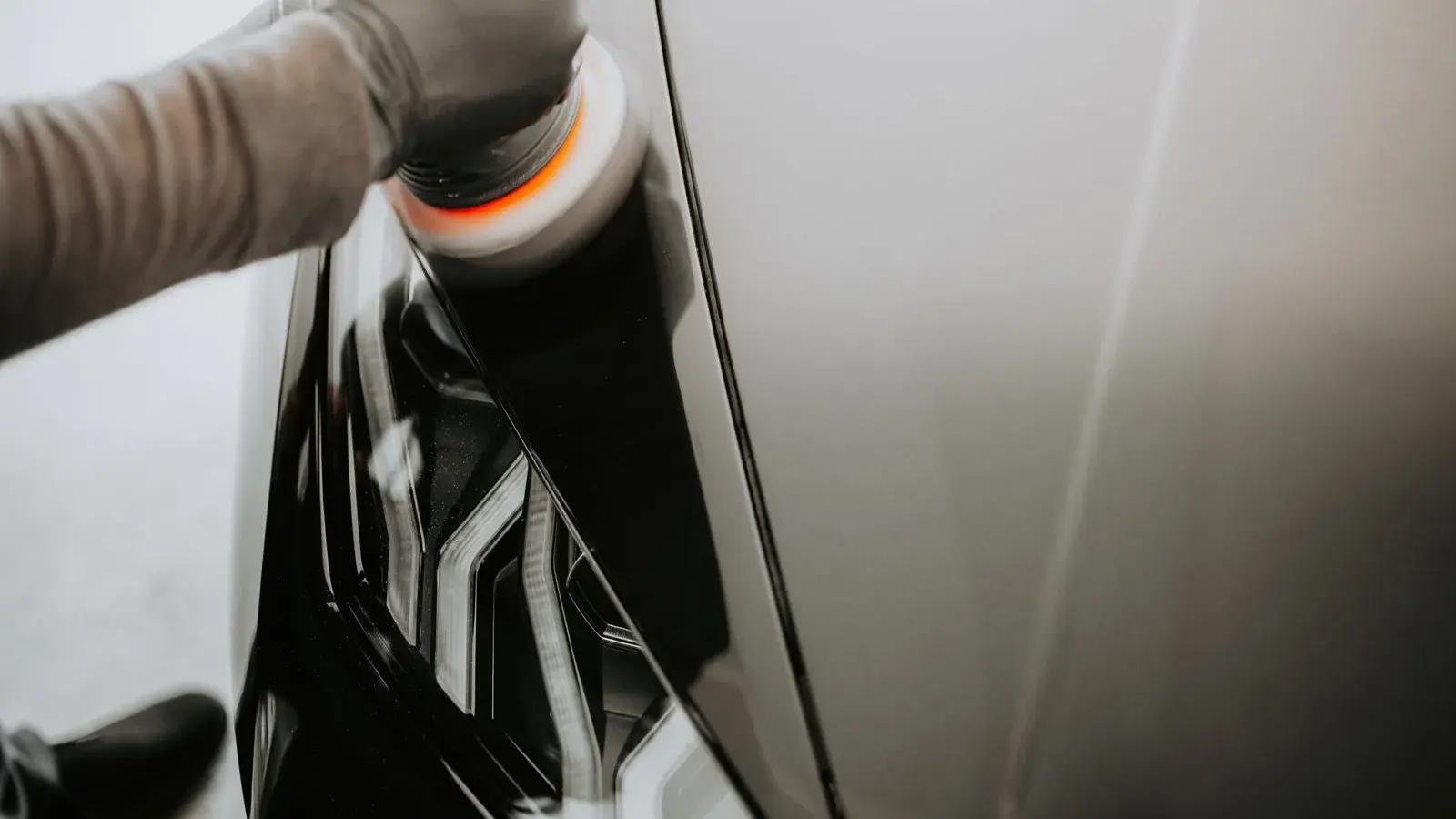 A gloved worker uses a machine polisher on a vehicle panel.