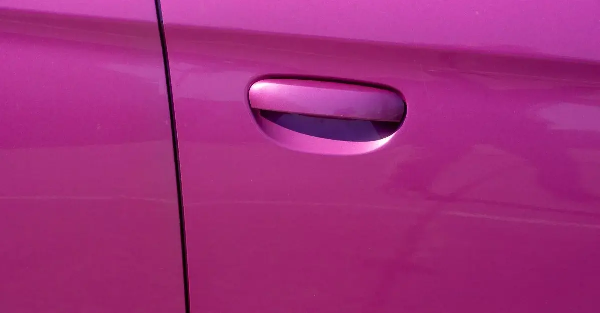 Close-up of a pink painted car door and handle.