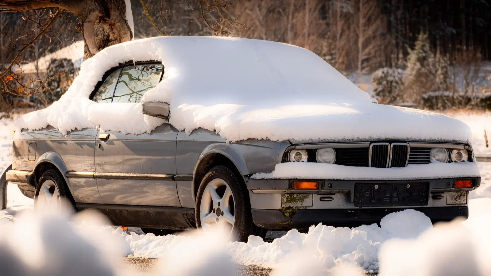 A parked BMW covered with snow on a winter street.