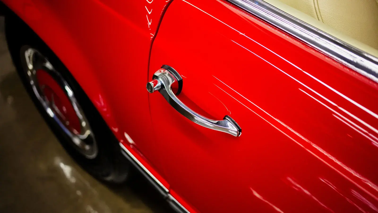Red car door with a chrome handle and reflected indoor lights.