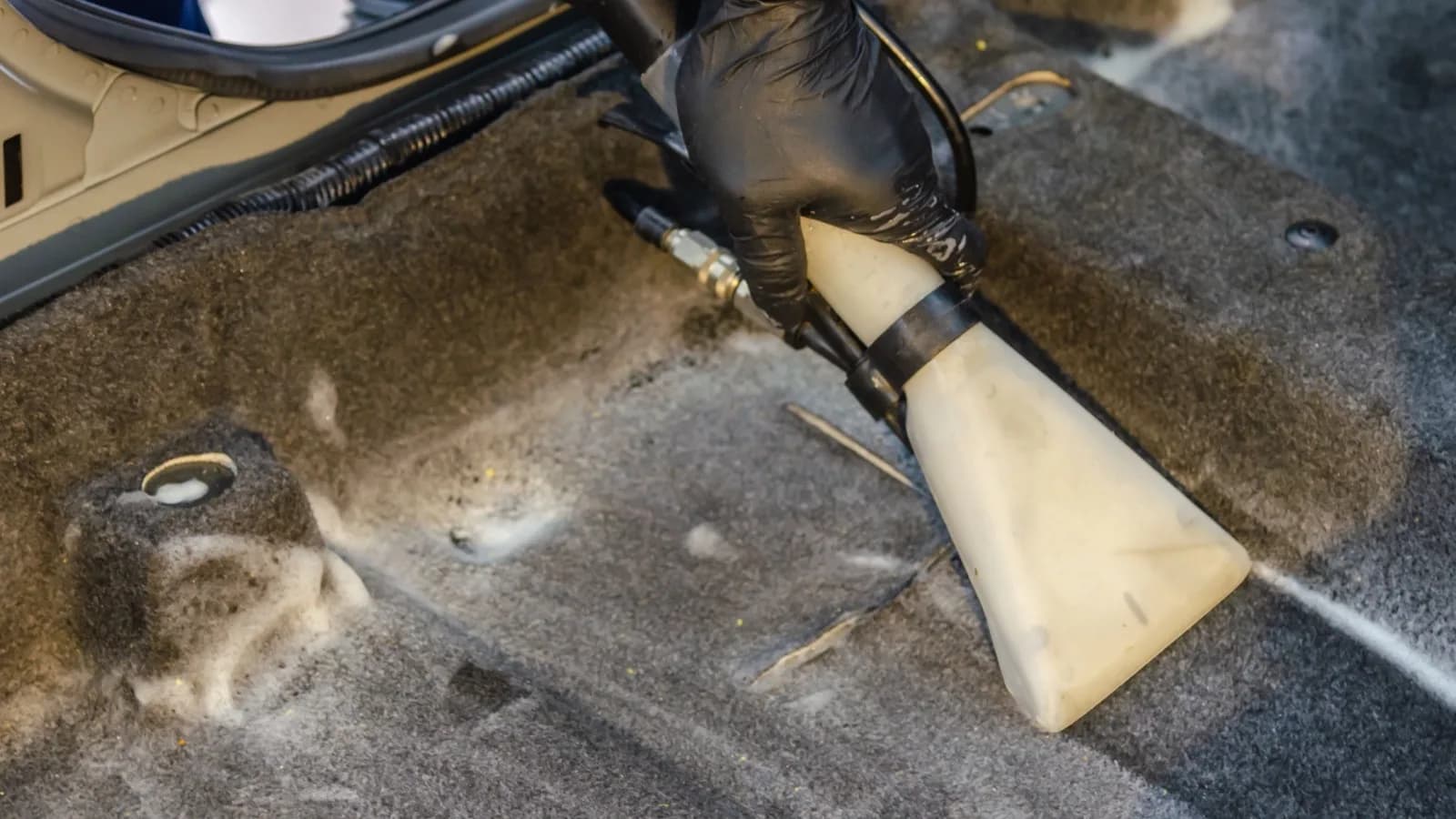 Photo by Khunkorn Laowisit on Pexels A gloved hand moves an upholstery extraction nozzle over vehicle carpet.