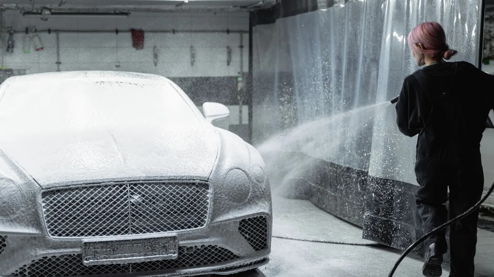 Photo by Tima Miroshnichenko on Pexels A worker sprays a foamed car in an indoor wash bay.