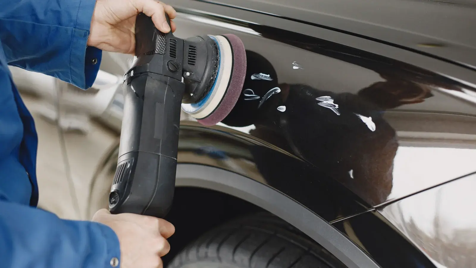 Photo by Gustavo Fring on Pexels Hands holding a dual action polisher with a foam pad against a dark car fender.