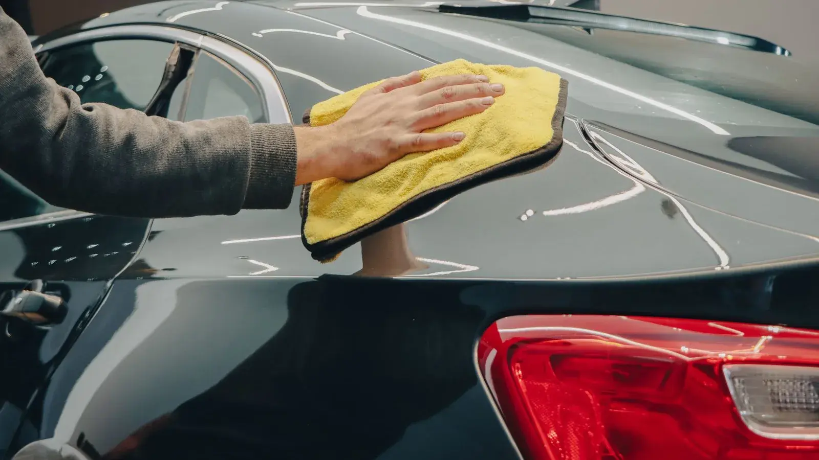 Photo by Dextar Studio ™ on Pexels A hand moves a yellow cloth across a dark car panel.
