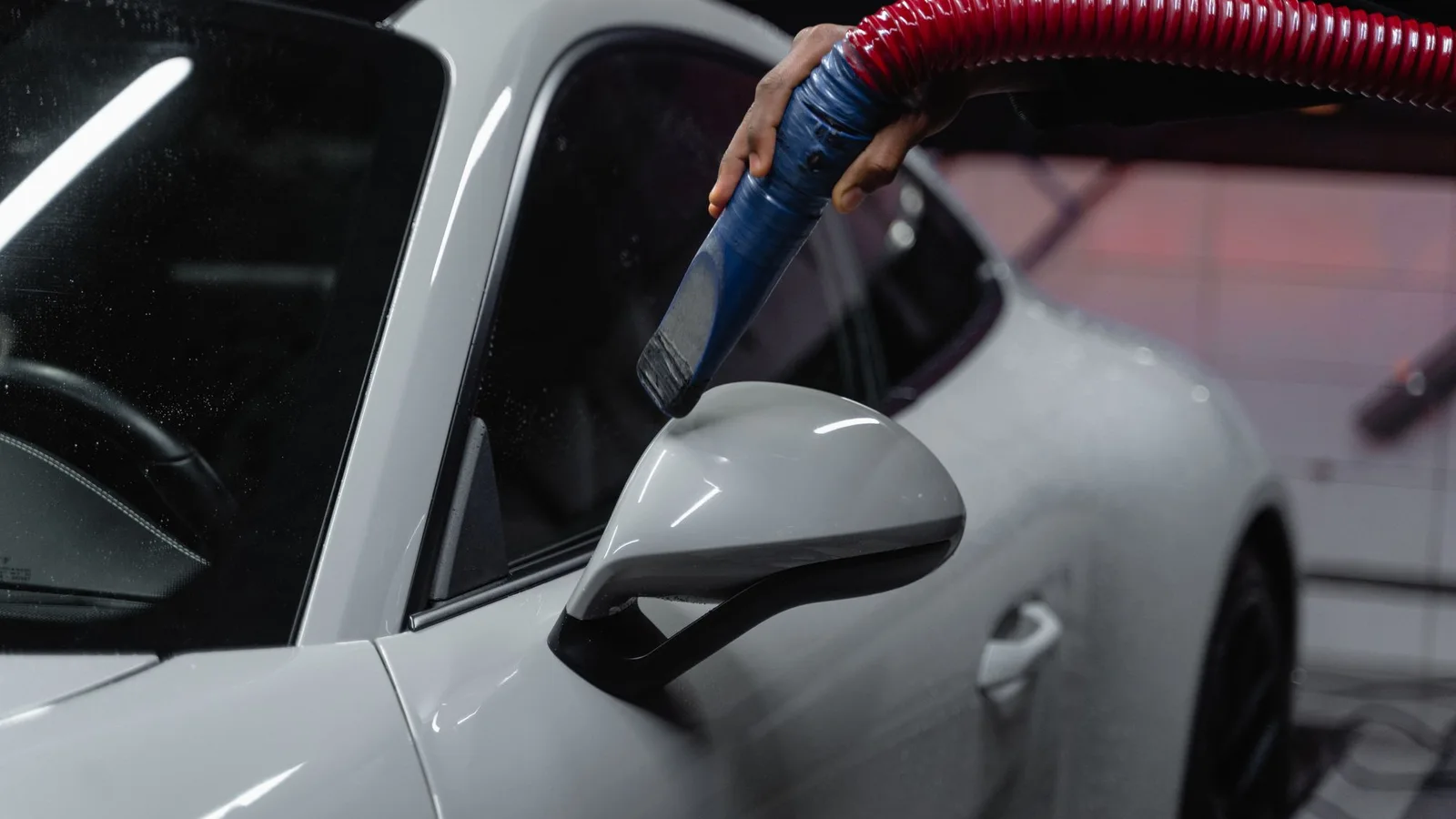 A hose nozzle held beside a white car’s side mirror.