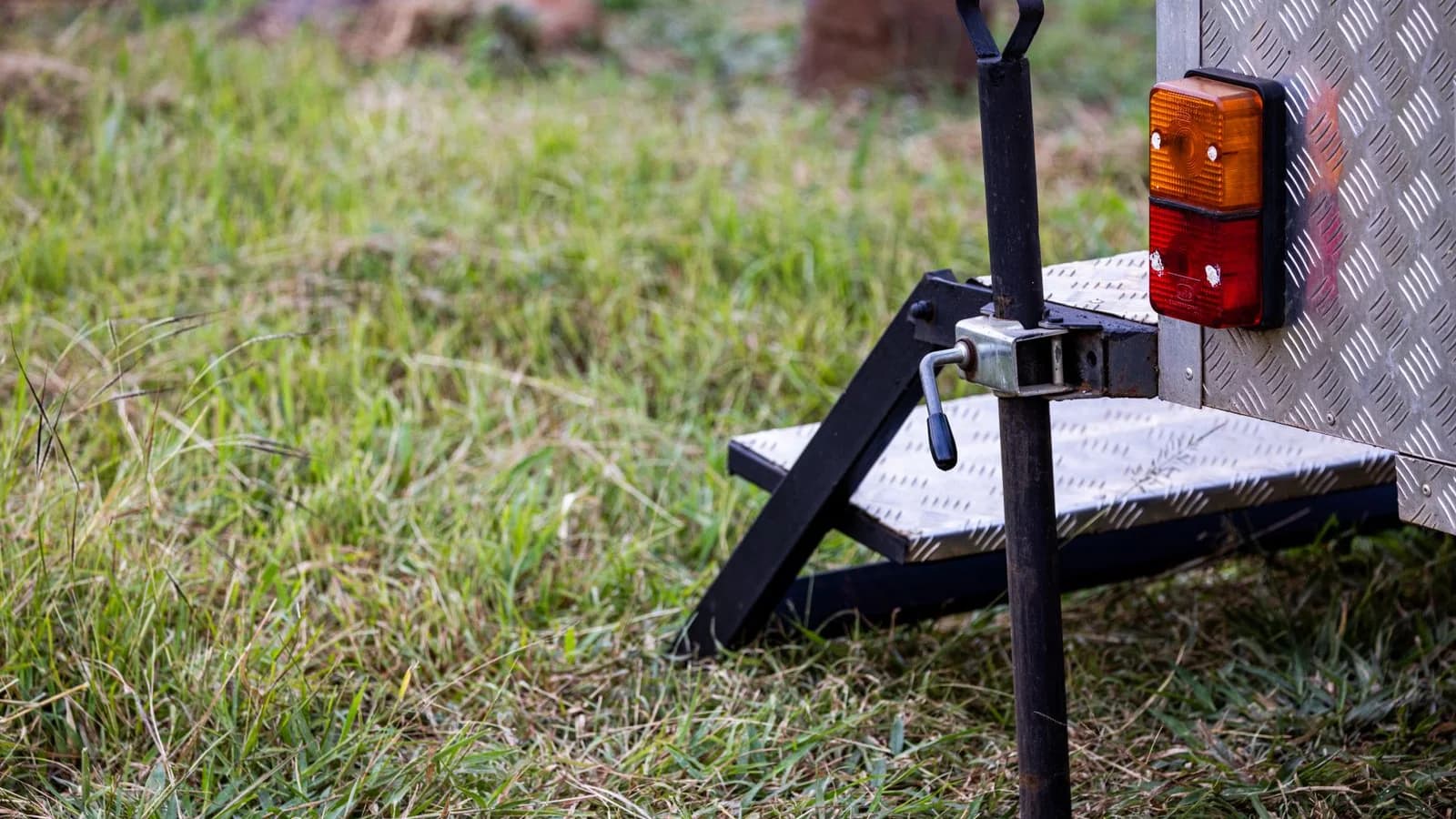 Photo by Magda Ehlers on Pexels Trailer jack and rear corner of a trailer on grass.