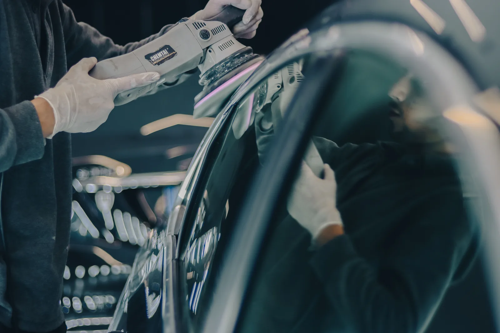Gloved hands holding a polisher against a car panel.