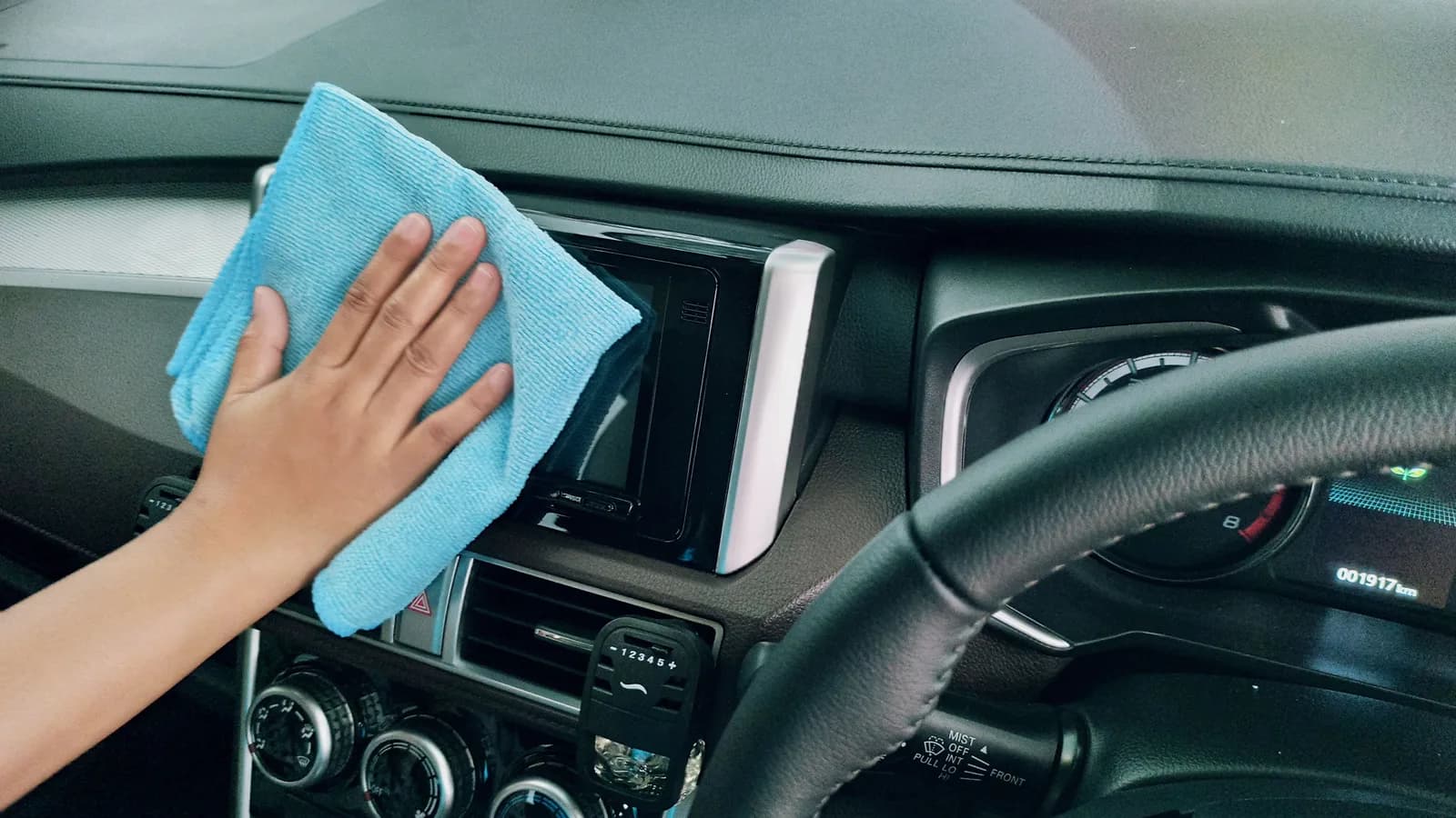 A hand wiping a car dashboard with a blue microfiber cloth.
