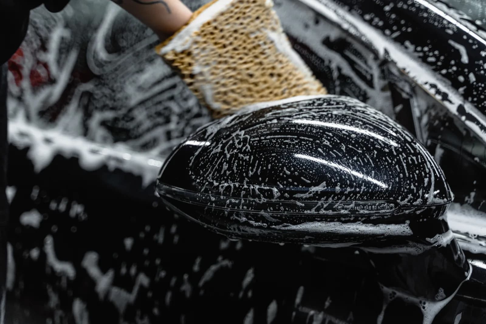A soapy sponge cleaning the area around a car mirror.